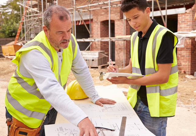 In this picture, an apprentice teaches a student at a construction site.